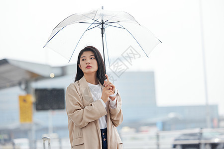 在机场室外撑伞等车的女性图片