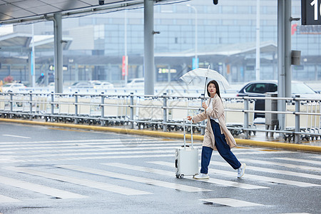 下雨天撑伞在机场外拉着行李的女性图片