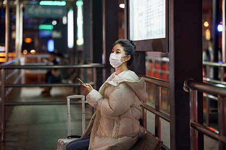 戴口罩的美女夜间出行坐在站台等待公交车图片