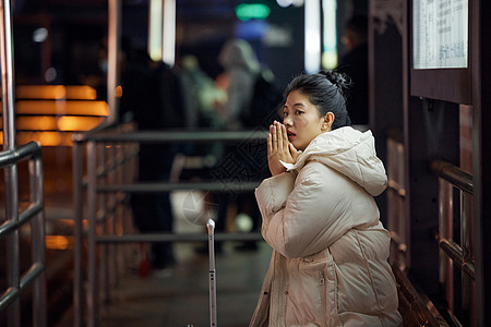 美女寒冬夜间出行坐在站台等待公交车高清图片