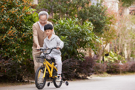 隔代抚养小区里爷爷教孙子骑自行车背景