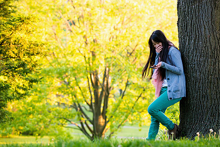 年轻女孩在公园里看着手机捂嘴偷笑图片