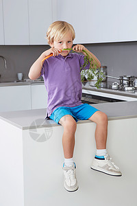 男孩坐在厨房操作台上闻胡萝卜叶图片