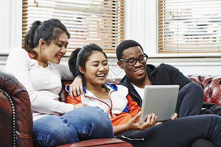 坐在沙发上的三个年轻成人看平板电脑图片
