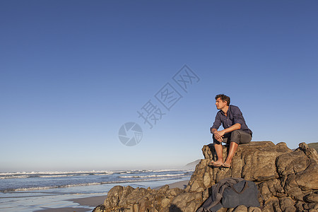 坐在海边岩石上的男人图片