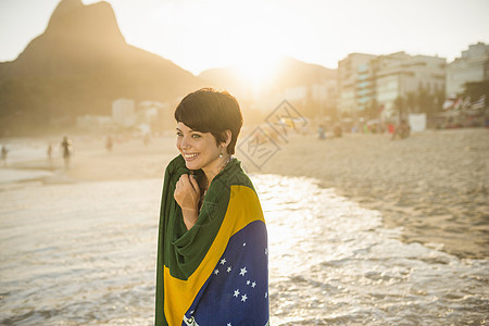 巴西伊帕内马海滩上包裹着巴西国旗的年轻女子图片