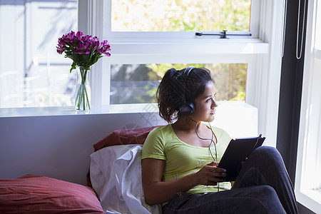 年轻妇女在床上戴着耳机使用平板电脑图片
