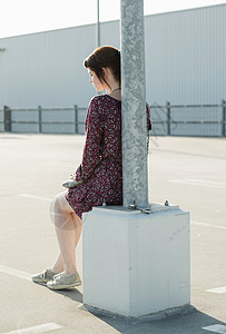 坐在空停车场灯柱旁边的年轻女士图片