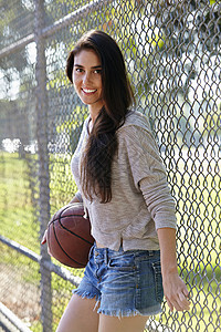 站在铁丝栅栏旁拿着篮球的年轻女子图片
