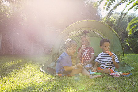 3名儿童在花园帐篷中吃冰棒背景图片