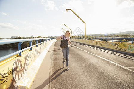 年轻女子在桥上低头单肩包图片