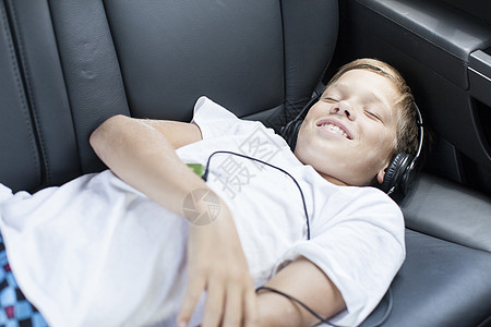 少年男孩在汽车后座听耳机时微笑图片