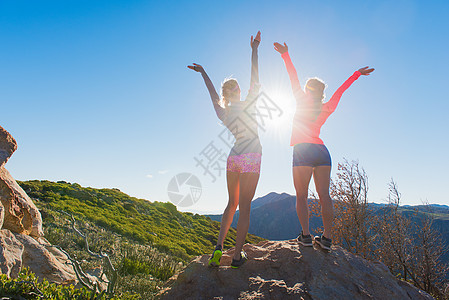 美国加利福尼亚州松树谷两位女跑步女子在太平洋顶峰步道的岩石上举手庆祝图片
