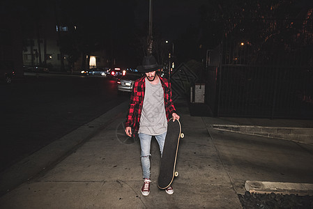 男生滑板运动员在夜间沿人行道走图片