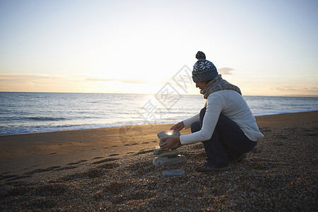 黄昏时在海滩边堆石头的年轻女性图片