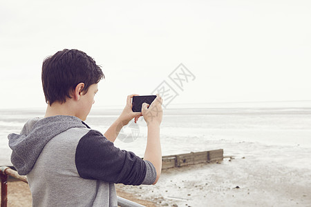 手机拍照用智能手机拍摄大海照片的少年男孩背景