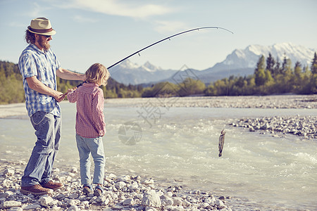 德国巴伐利亚州瓦尔高一对中年男子和一对男孩拿着鱼竿在河边钓鱼图片