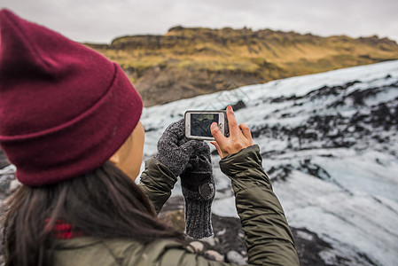 在冰岛Solheimajokol使用智能手机上拍摄冰川的女游客图片