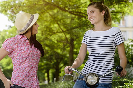 骑自行车的年轻女子与戴巴拿马帽的年轻女交谈图片