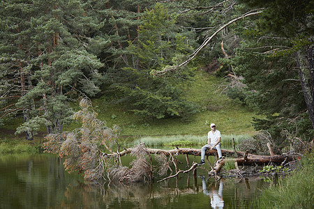 男子坐在一棵栽倒在湖上的树上休息图片