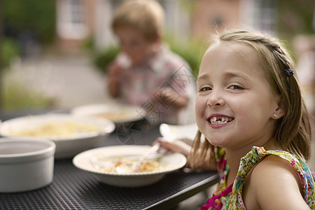 女孩在花园桌前吃饭仰望肩对着镜头微笑图片