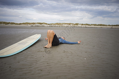 中老年女人在沙上放松坐在她旁边的冲浪板上图片