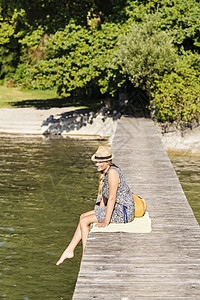 德国巴伐利亚州阿默西市肖多夫一名戴着巴拿马帽的年轻女子坐在木码头上眺望远方图片