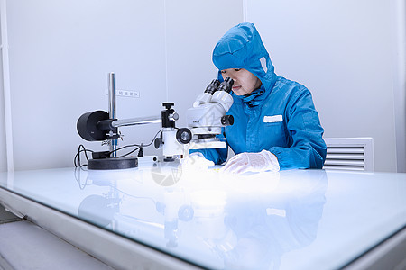 在灵活电子设备工厂清洁室使用显微镜的女工图片