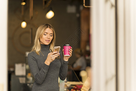 使用智能手机带外送咖啡的妇女图片