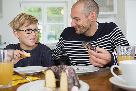 成人中年男子和儿在厨房餐桌上吃蛋糕图片