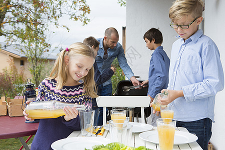 女孩和兄弟在花园烧烤桌上倒果汁背景图片