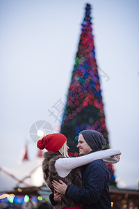 在圣诞树前甜蜜拥抱的年轻情侣图片