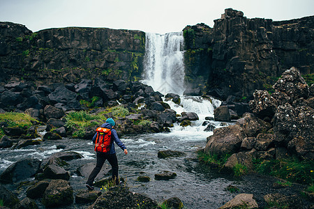 河边岩石上站立着背包的成年女子看着冰岛瀑布图片