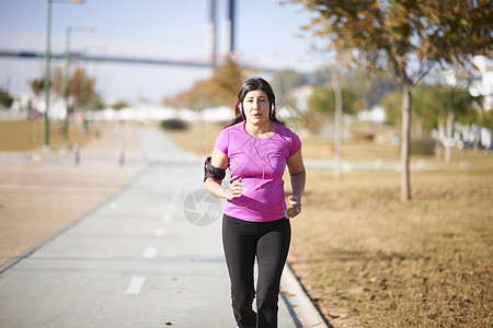 身戴耳机在路上慢跑的成年妇女图片
