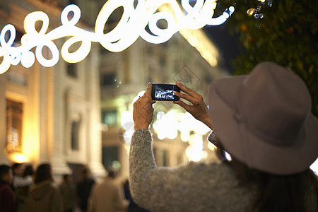 街上妇女拿手机拍装饰灯图片