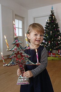 抱着圣诞饰品的女孩在圣诞节树前看着镜头微笑图片