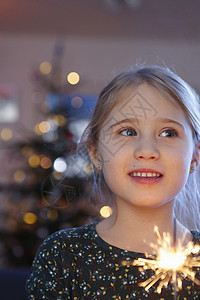 女孩在圣诞树前拿着烟花看镜头微笑图片