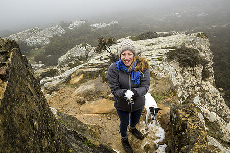 女徒步旅行者和她的宠物狗在迷雾山中拿着雪球图片