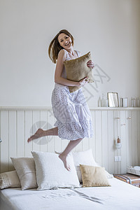 穿着白色裙子在床上跳跃的年轻女性图片