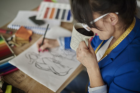 在设计工作室喝咖啡画时装设计草图的女人图片