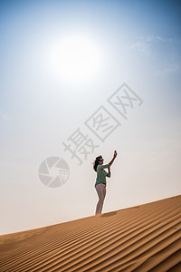 阿拉伯联合酋长国迪拜在沙漠丘上使用智能手机自拍的女游客图片