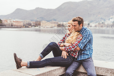 坐在意大利科莫湖港口墙抱着的青年夫妇图片