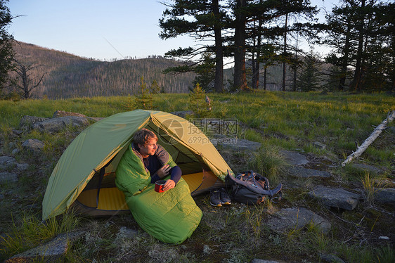 美国华盛顿州科尔维尔森林公园午夜山脊上一名男子坐在睡袋里看日落图片