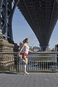 在美国纽约市威廉斯堡大桥下户外运动伸展活动的年轻女子图片