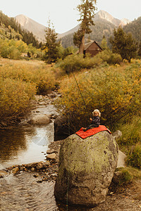 小男孩坐在小溪边的岩石上钓鱼图片