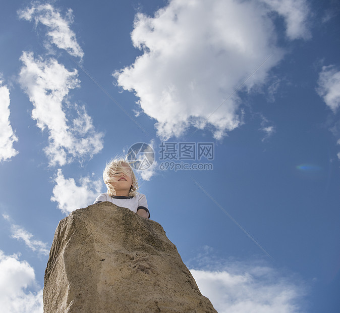 男孩在岩石的顶上向远看图片