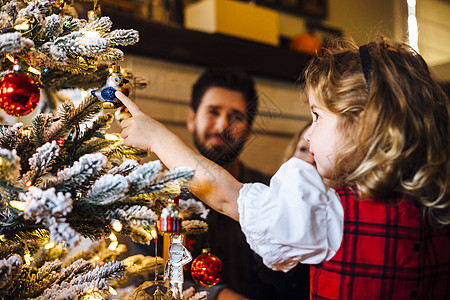 蹒跚学步的女婴给父母指着圣诞树上的装饰品图片