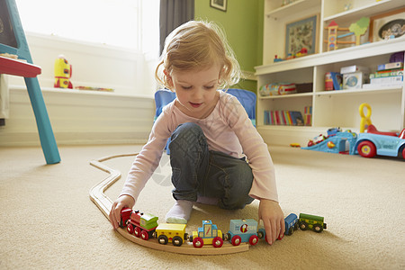 在游戏室地板上玩火车的女幼儿背景图片