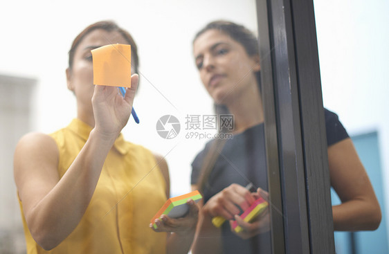 两名女商人在办公室玻璃墙上贴粘纸条图片
