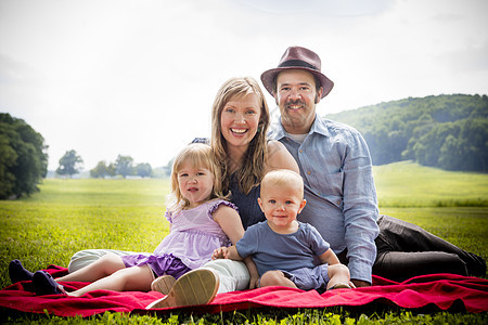 与女儿和子一起坐在野餐毯子上的中成年夫妇肖像图片